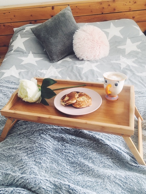 pancakes and coffee on tray, sat on bed with cushions in background